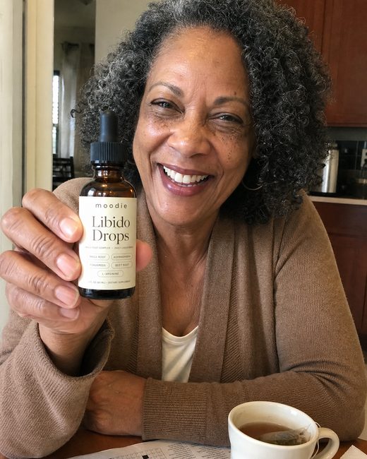 Moodie customer, 63, kitchen table, holding her bottle of Libido Drops